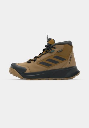 Brown hiking boot with a black rubber toe cap, textured midsole, and mesh upper. Features three black stripes on the side and gray collar.