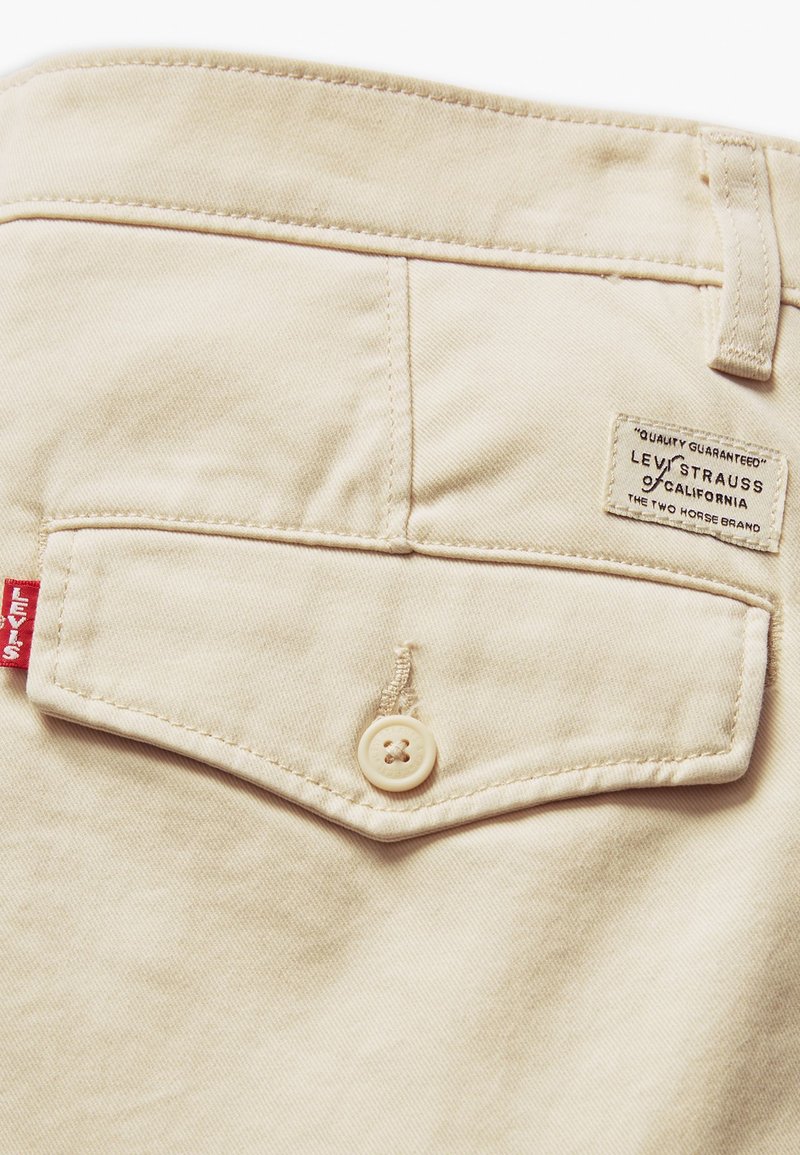 Poche de pantalon en denim beige avec fermeture à bouton, étiquette Levis Strauss et détails de couture subtils sur le tissu.