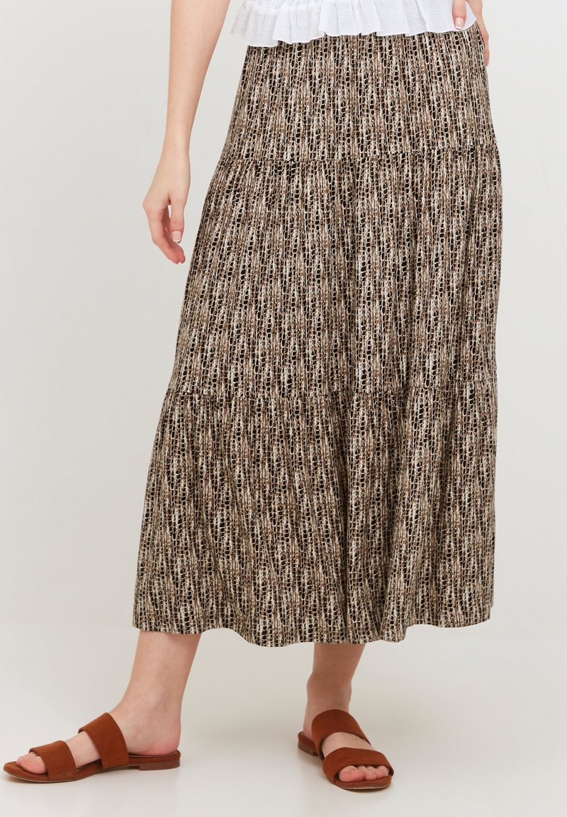 Femme portant une jupe midi à motifs dans des tons marron et beige, associée à des sandales plates marron et un haut blanc.