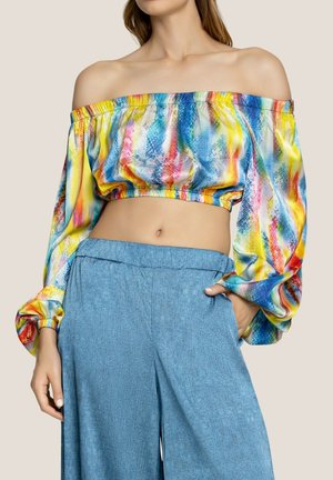 Top corto off-the-shoulder con un motivo astratto multicolore, caratterizzato da maniche ampie e orlo elasticizzato. Abbinato a pantaloni larghi blu chiaro.