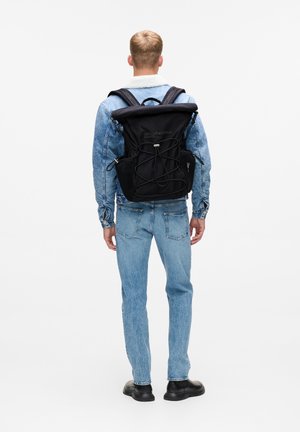 Zaino nero con chiusura roll-top, cordino anteriore e tasche laterali in rete. Il tessuto presenta una texture liscia con dettagli di branding.