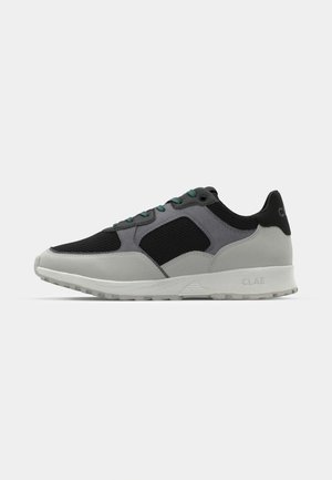 Zwarte en grijze sportschoenen met een bovenwerk van mesh, een gladde rubberen buitenzool, groene veters en CLAE-branding op de hiel.