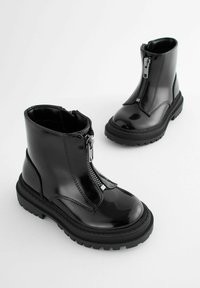 Stivaletti in pelle verniciata nera con zip frontale, punta arrotondata, suola in gomma spessa e dettagli di cucitura minimal.