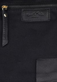 Schwarze Stoffoberfläche mit schwarzem Leder-Reißverschlussanhänger und einem aufgenähten Lederetikett mit Prägung "Seventh Code Studio."
