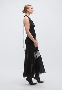 Rochie neagră cu gât halter, cu design strâns, material transparent și o despicătură înaltă pe coapsă. Asortată cu tocuri negre ascuțite și o poșetă mică și sclipitoare.