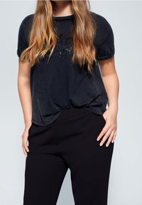 T-shirt noir à manches courtes avec une coupe ample et un design graphique texturé. Associé à un pantalon noir sur-mesure, mettant en valeur un look décontracté.
