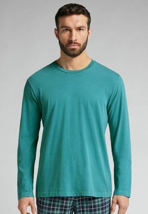 Türkises Langarm-T-Shirt aus weichem, leichtem Baumwollstoff. Mit rundem Halsausschnitt und lockerer Passform, getragen zu karierten Schlafanzughosen.