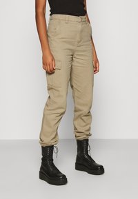 Beige cargo kalhoty mají zúžené nohavice, boční kapsy a standardní pas. Vytvořte kontrast s černými šněrovacími bojovými botami.