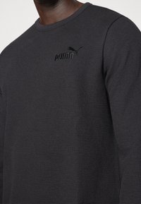 Schwarzes Waffelstrick-Sweatshirt mit Rundhalsausschnitt, ausgestattet mit einem geprägten Puma-Logo auf der Brust. Strukturierter Stoff mit langen Ärmeln.