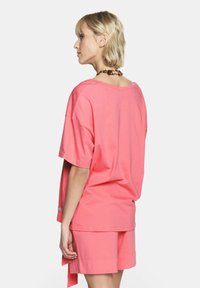 Przestrzenna koralowo-różowa koszulka z okrągłym dekoltem i krótkimi rękawami, w zestawie z pasującymi szortami; wykonana z miękkiego, oddychającego materiału.