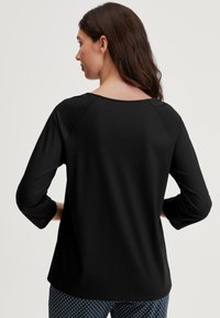 Zwarte langemouwen top met een ronde halslijn en raglan mouwen, gemaakt van een gladde, zachte stof en met een ontspannen pasvorm.