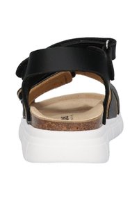 Sort lædersandal med krydsremme, en korkfodsål og en hvid gummisål. Inkluderer en justerbar rygrem for bedre pasform.