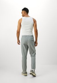 Gray lightweight pants with elastic waistband and back pocket. Worn with a white tank top and gray sneakers, standing against a white background.