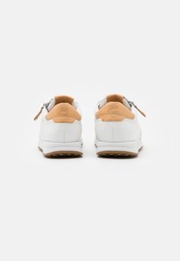 Chaussures en cuir blanc avec des accents en daim beige et des semelles en caoutchouc texturé, dotées de fermetures éclair sur les côtés et d'un logo en relief sur le talon.