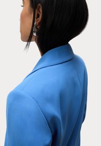 Blauwe op maat gemaakte blazer met gestructureerde schouders, een soepele textuur en een gesneden revers, met een slank ontwerp en gestikte details.