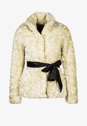 Crème-kleurige nepbonten jas met hoge kraag, gecombineerd met een witte top en donkerblauwe spijkerbroek. Een zwarte handtas en enkellaarzen maken de look compleet.