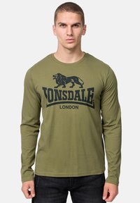 Olívazöld, hosszú ujjú, környakú pamut póló. Elöl fekete oroszlán grafika és "LONSDALE LONDON" felirat található.