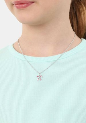 Persona che indossa una collana d'argento con un piccolo ciondolo a forma di fiocco rosa e argento su una maglietta azzurro chiaro a coste.