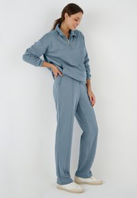 Sudadera de cremallera azul claro con cuello alto, combinada con pantalones jogger a juego. Ambos están hechos de una tela suave con una textura lisa.