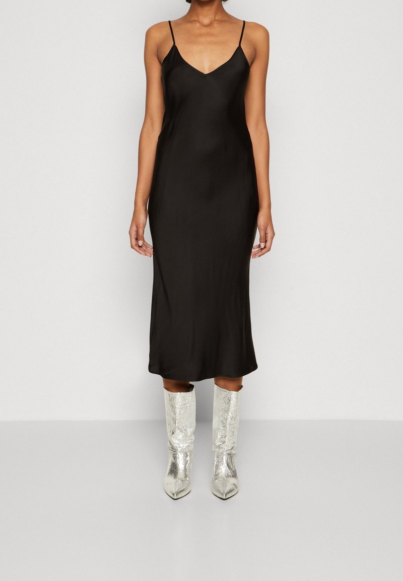 Zwarte satijnen slipdress met dunne banden en een knielange snit. Gecombineerd met glanzende zilveren kniehoge laarzen met een spitse neus.