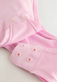 Lichtroze katoenen kledingstuk met een gladde textuur, voorzien van roze drukknoopsluitingen en satijnachtige stofdetails op de manchetten.