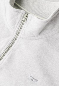 Grijze sweater met rits gemaakt van zacht stof, met een geribbelde kraag, zilveren rits en geborduurd logo op de linkerborst.