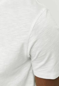 Fehér, rövid ujjú póló, puha, textúrált anyagból. Az eseményeken látható varrás a gallér és a ujj szélén. Simaság és könnyedség jellemzi az anyagot.