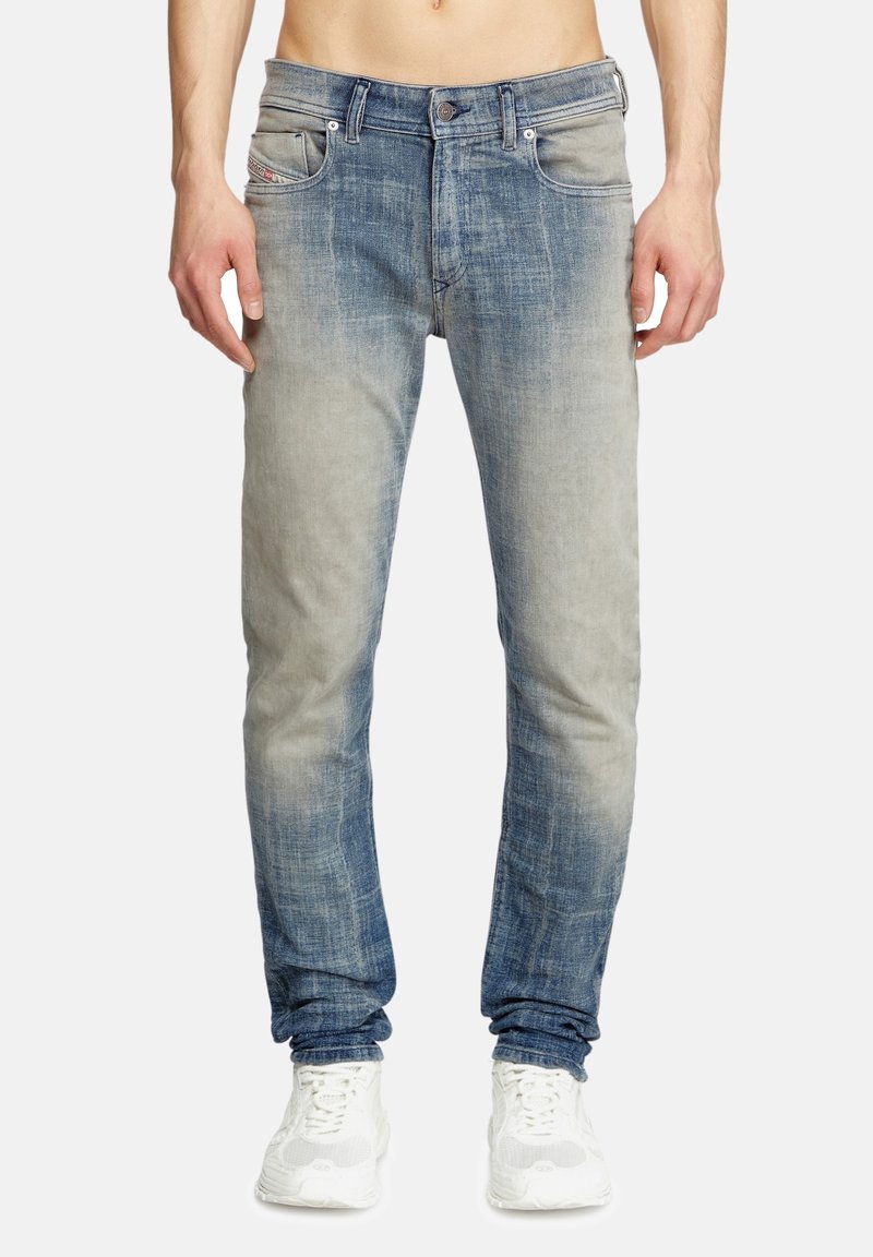 Jeans en denim dégradé allant du gris clair au bleu foncé, avec cinq poches, des coutures visibles et une coupe slim. Portés avec des baskets blanches.