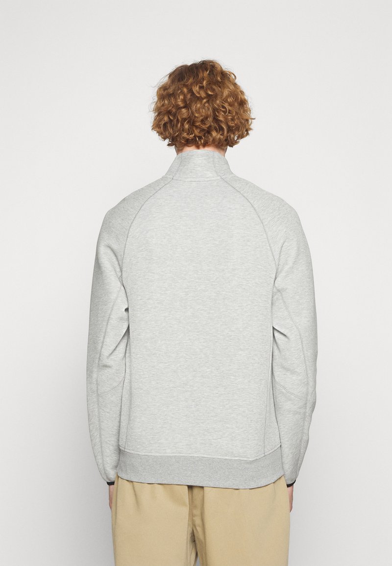 Sweatshirt zippé gris clair avec un col montant, des poignets et un ourlet côtelés. Tissu doux et texturé ; il présente des manches raglan pour une plus grande liberté de mouvement.