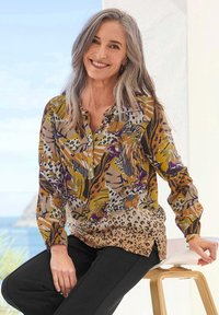 Langärmlige Bluse mit einem bunten floralen und Tiermuster in Braun-, Lila- und Grüntönen; leichtes Material, Knopfverschluss vorne.