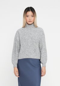 Pulover din tricot cu guler înalt, de culoare gri deschis, cu un model texturat, având umeri căzuți și o croială scurtă, asortat cu o fustă din satin de culoare albastru închis.