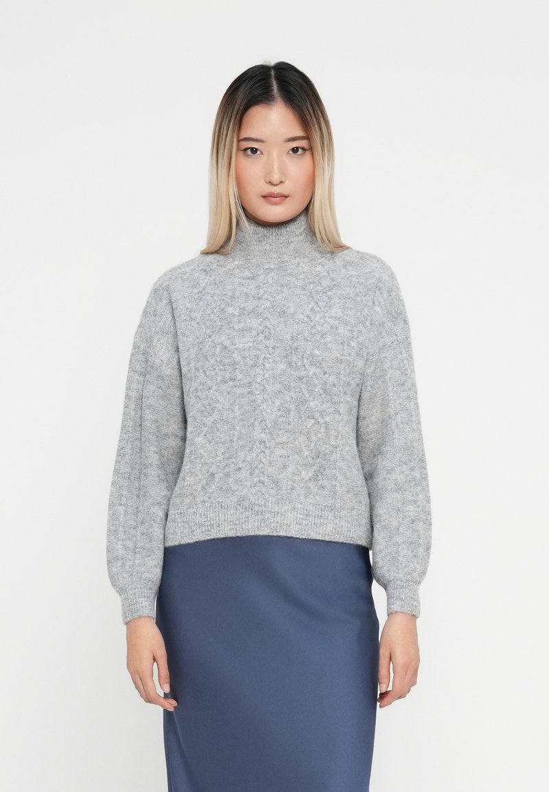 Pulover din tricot cu guler înalt, de culoare gri deschis, cu un model texturat, având umeri căzuți și o croială scurtă, asortat cu o fustă din satin de culoare albastru închis.