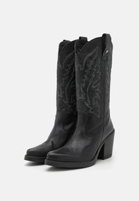 Bottes de cowboy en cuir noir avec des détails brodés, un bout pointu et un talon bloc. Équipées de languettes pour un enfilage facile.