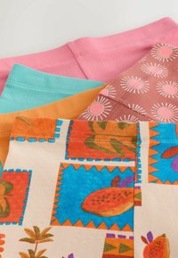 Pile de morceaux de tissu pliés colorés avec du rose uni, turquoise, moutarde, des motifs imprimés de soleil marron et des motifs multicolores de fruits tropicaux et de feuilles.