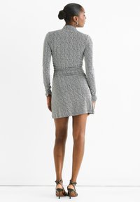 Long-sleeve, fitted dress in a textured black and white knit. Features a mid-thigh length and sleek back design, paired with strappy heels.