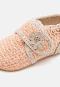 Svītroti iekštelpu apavi mīkstā korallā un beidžā tekstilā, ar velcro siksniņu un zieda akcentu ar spīdīgu centru. Apaļas pirksta formas dizains.