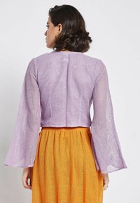 Lavender, cropped knit top with long flared sleeves. The texture is open-weave. Paired with a bright orange, pleated skirt.