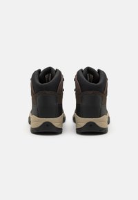 Brown and black mid-cut hiking shoes featuring synthetic materials, textured accents, and a beige rubber outsole with patterned tread.