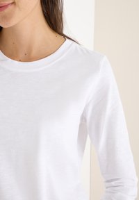 Camiseta de algod�ón blanca de manga larga con cuello redondo, textura suave y diseño minimalista, adecuada para el uso casual.