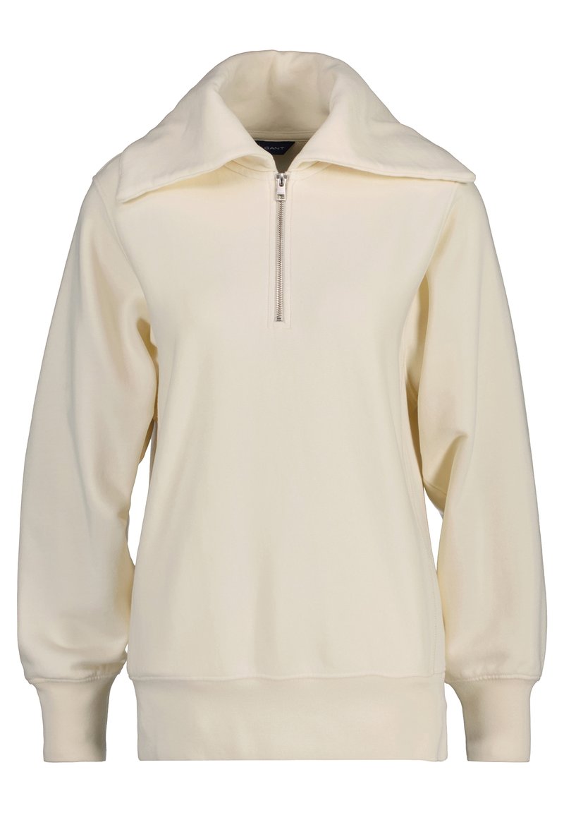 Felpa crema chiara con colletto alto, zip frontale e polsini a costine. Tessuto liscio con una vestibilità rilassata e design minimalista.