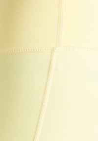 Nahaufnahme von blassgelben Stoffpanelen mit sichtbarer Overlocknaht, die ein Kreuzmuster bildet.