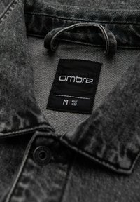 Camicia di denim nera con una texture morbida, dotata di colletto, chiusura a bottoni e un'etichetta interna con la scritta "ombre" e taglia M, EUR 48.