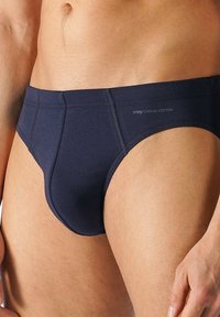 Mörkblå bomullshängsel med en slät ytstruktur, elastisk midja och kontrasterande sömmar. Har en logotyp på framsidan.