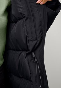 Zwart pufferjack interieur met doorgestikte secties, trekkoordversteller en zakken. Glad stof met subtiele patronen.