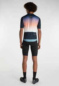 Pánska cyklistická dres s prechodovými farbami od námorníckej modrej po broskyňovú, s krátkymi rukávmi a so zipsom na zadnej strane. Nosené s čiernymi cyklistickými šortkami.