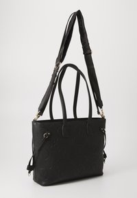 Black tote bag made of textured synthetic material, featuring embossed floral and logo patterns, dual handles, and a detachable shoulder strap.