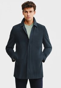 Granatowy płaszcz zewnętrzny o eleganckim, minimalistycznym designie. Posiada kołnierz mandaryński, długie rękawy oraz zamek błyskawiczny, wykonany z gładkiego materiału.