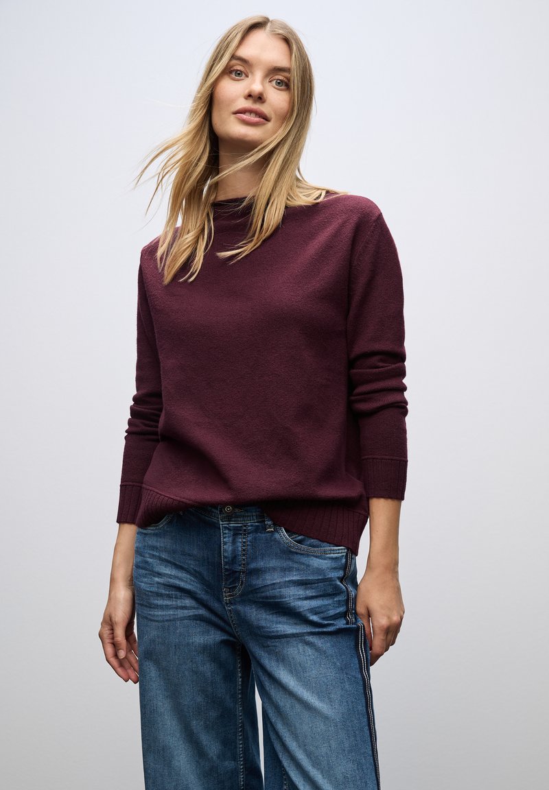 Burgunderfarbener Strickpullover mit gerippten Bündchen und Saum, kombiniert mit weiten blauen Jeans aus Denim mit seitlichen Streifen. Schlichter und strukturierter Designstil.