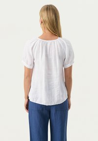 Weiße Leinenbluse mit puffärmeln und gerafft Neckline, kombiniert mit blauen Leinenhosen in einer lockeren, lässigen Passform.