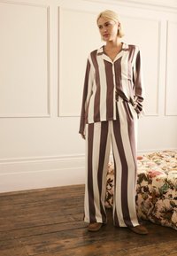 Gestreiftes Pyjama-Set in tiefem Mauve und Creme, bestehend aus einem knöpfbaren Oberteil mit Tasche und locker sitzenden Hosen mit elastischem Bund.